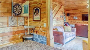 Interno di una baita di legno con una bacheca da freccette, un quadro incorniciato, un divano e un muro in pietra.