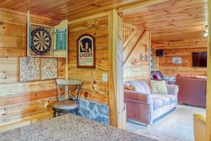 A wooden cabin interior with a dartboard, a framed picture, a couch, and a stone wall. - Bear Bottoms Welcome (Whittier)