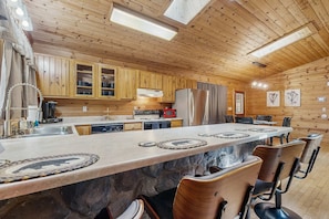 A wooden cabin interior with a kitchen, dining area, and bar seating. - Maggie Valley cabin with wrap around porch & gorgeous mountain views (Maggie Valley)
