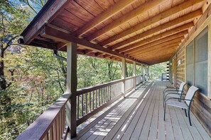 A covered wooden deck with chairs, overlooking a forested area. - Maggie Valley cabin with wrap around porch & gorgeous mountain views (Maggie Valley)