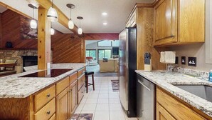 Una cocina con gabinetes de madera, encimera de granito, refrigerador de acero inoxidable, luces colgantes y chimenea de piedra.