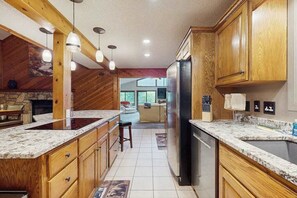 Eine Küche mit Holzschränken, einer Granit-Arbeitsplatte, einem Edelstahl-Kühlschrank, Pendelleuchten und einem Kamin aus Naturstein.