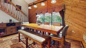 Un comedor con mesa de madera, bancos y una araña.