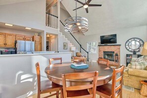 A dining area with a round table and chairs, a kitchen with wooden cabinets, a staircase, a fireplace, and a television on the wall. - Cozy home with wraparound deck, fireplace, AC, & W/D (Waynesville)