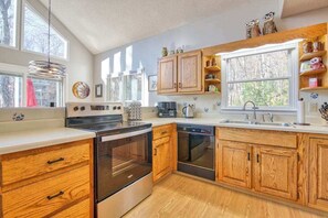 A modern kitchen with wooden cabinets, stainless steel appliances, and large windows. - Cozy home with wraparound deck, fireplace, AC, & W/D (Waynesville)