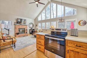 A spacious kitchen with a large stove, a brick fireplace, and a dining area with a chair and table. - Cozy home with wraparound deck, fireplace, AC, & W/D (Waynesville)