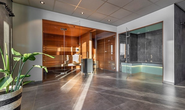 Eine moderne Lobby mit einer Rezeption, einem durch Glasabgrenzung gekennzeichneten Duschbereich und einer Topfpflanze.