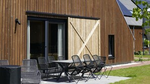 En moderne træbygning med stor skydedør, udendørs siddeområde og solpaneler på taget.