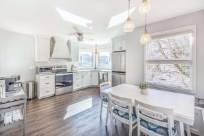 A modern kitchen with white cabinetry, a dining area with a white table and chairs, and a large window providing a view of the outdoors. - The Willows (Waynesville)