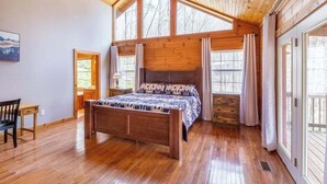 Un dormitorio con techo de madera, una cama, una ventana y una puerta.