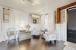 Ein Zimmer mit Holzboden, weißen Wänden, einem Kamin und einer Decke mit freiliegenden Balken.