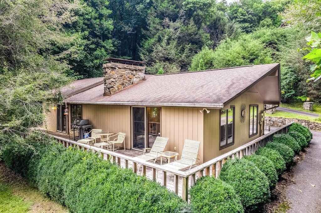 Eine Holzhütte mit einer Terrasse, einem Steinkamin und Blick auf den Wald.