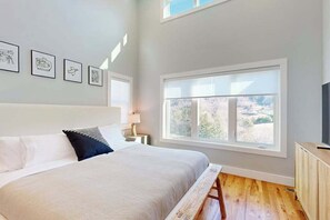 Ein Schlafzimmer mit Bett, Nachttisch, Lampe, Fenster und gerahmten Bildern an der Wand.