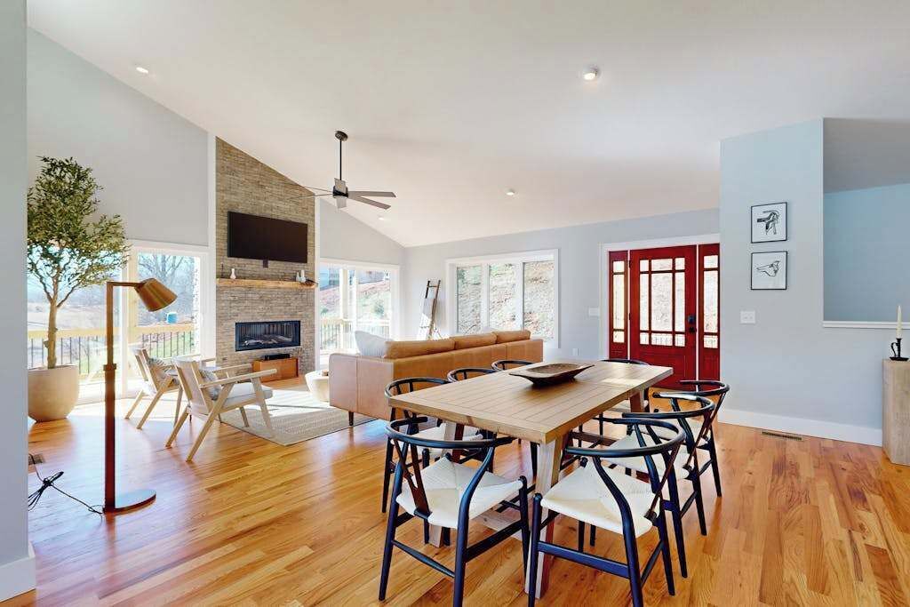 Un vaste espace de vie comprenant une table à manger en bois, des chaises modernes, une cheminée et une grande fenêtre.