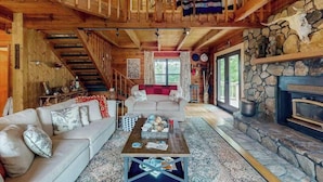A log cabin interior with a fireplace, a sofa, a coffee table, and a staircase. - Walela Cabin (Topton)