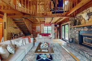 Ein Holzblockhaus-Innenraum mit Kamin, einer Couch, einem Couchtisch und einer Treppe.