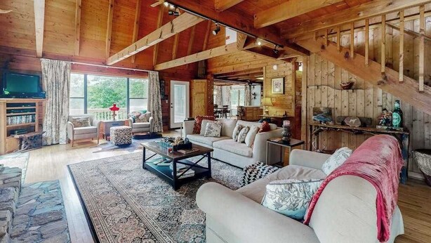 A spacious living room with a high ceiling, wooden beams, a fireplace, and a television. - Walela Cabin (Topton)