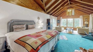 A bedroom with a large bed, a wooden ceiling, and a view of the outdoors through a window. - Walela Cabin (Topton)