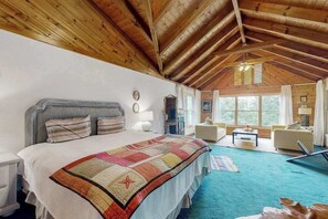 Ein Schlafzimmer mit einem großen Bett, einer Holzbalkendecke und Blick ins Freie durch ein Fenster.