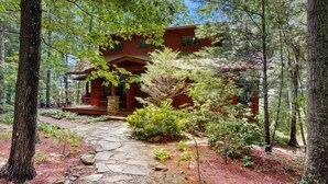 A cabin with a stone pathway leading to the entrance, surrounded by dense forest. - Eagles Wing Lodge | Game Room, Firepit, Dazzling Sunset Views | Near Downtown (Asheville)