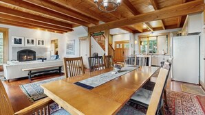 A spacious dining area with a long wooden table, surrounded by chairs, and a fireplace in the background. - Eagles Wing Lodge | Game Room, Firepit, Dazzling Sunset Views | Near Downtown (Asheville)