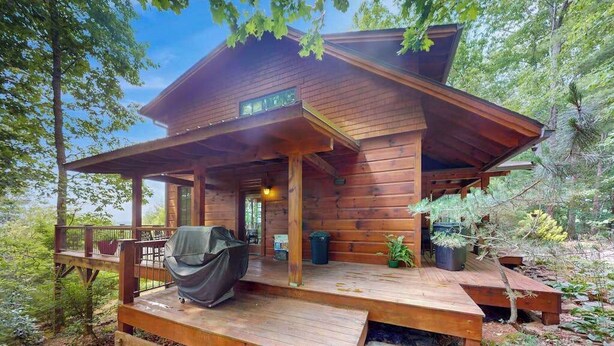 A wooden cabin with a covered porch, a grill, and potted plants. - Eagles Wing Lodge | Game Room, Firepit, Dazzling Sunset Views | Near Downtown (Asheville)