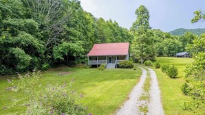 A house with a red roof, surrounded by lush greenery and a gravel path leading to it. - Pebble on the Creek (Whittier)
