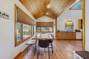 Eine moderne Küche mit Holzausstattung, einem Essbereich mit Holztisch und -stühlen sowie großen Fenstern mit Jalousien.