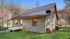 A small wooden cabin with a metal roof, a front porch, and a small deck. - Pebble on the Creek (Whittier)