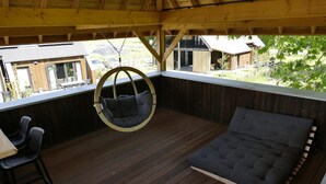 Un área de estar al aire libre techada con una silla colgante, un banco acolchado y una mesa con sillas.