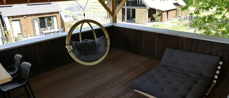 Un área de estar al aire libre techada con una silla colgante, un banco acolchado y una mesa con sillas.