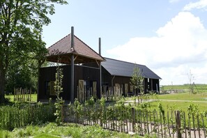 A rustic building with a sloped roof, wooden structure, and a fenced garden area. - Lennepserf - De Bok (Veessen)