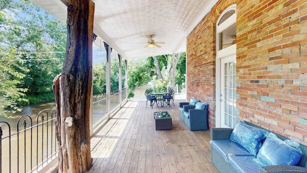 Eine überdachte Terrasse im Freien mit Holzdeck, Ziegelwand und einer Sitzecke mit Sofa und Sesseln.