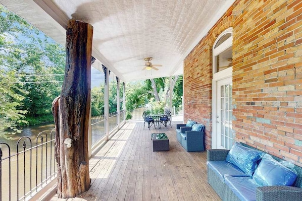 Eine überdachte Terrasse im Freien mit Holzdeck, Ziegelwand und einer Sitzecke mit Sofa und Sesseln.