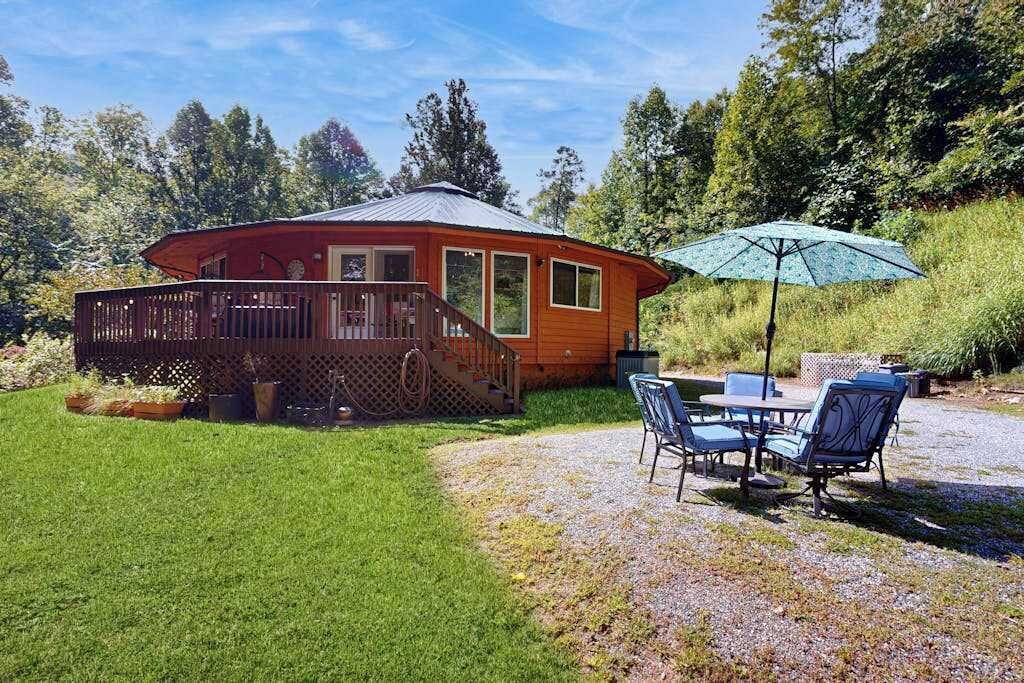 A wooden cabin with a deck, a patio with chairs and a table, and a green umbrella.