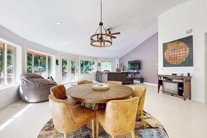 A spacious living room with a round wooden table, comfortable seating, a large window, and a modern ceiling light. - Circle House in the Smoky Mountains (Whittier)
