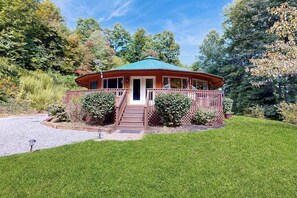 A wooden cabin with a green roof, surrounded by a wooden deck and a gravel path leading to the entrance. - Circle House in the Smoky Mountains (Whittier)