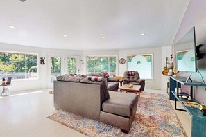 A spacious living room with a large sofa, a smaller armchair, a coffee table, and a television on a stand. - Circle House in the Smoky Mountains (Whittier)
