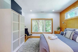 A bedroom with a bed, a chair, a window, and a wardrobe.