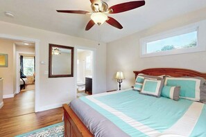 Ein Schlafzimmer mit einem Bett, einem Deckenventilator, einem Fenster und einer Tür zu einem anderen Raum.