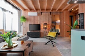 A modern living room with a sofa, a coffee table with a vase, a TV, and a chair with a cushion. - Lennepserf - De Horstjes (Veessen)