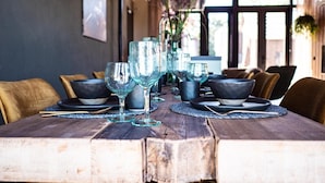 Una mesa de comedor de madera con cristalería y cuencos negros, ubicada en una habitación con vigas de madera y vistas amplias por ventanas grandes.