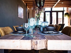 A wooden dining table with glassware and black bowls, set in a room with wooden beams and a view through large windows. - Lennepserf - De Horstjes (Veessen)