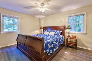 A bedroom with a wooden bed, two bedside tables, a ceiling fan, and two windows with blinds. - Dog-friendly home with large yard, lawn games, firepit, screened porch, & AC (Asheville)