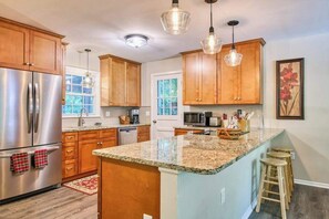 A kitchen with wooden cabinets, stainless steel appliances, granite countertops, and pendant lighting. - Dog-friendly home with large yard, lawn games, firepit, screened porch, & AC (Asheville)