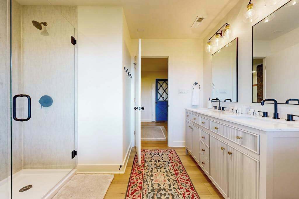 Un baño moderno con cabina de ducha, un espejo grande y un tocador blanco con varios lavamanos.