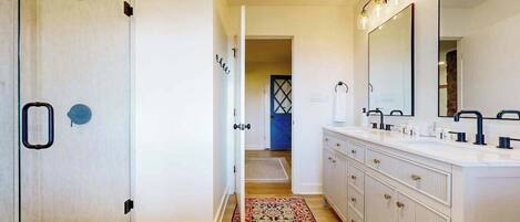 Un baño moderno con cabina de ducha, un espejo grande y un tocador blanco con varios lavamanos.