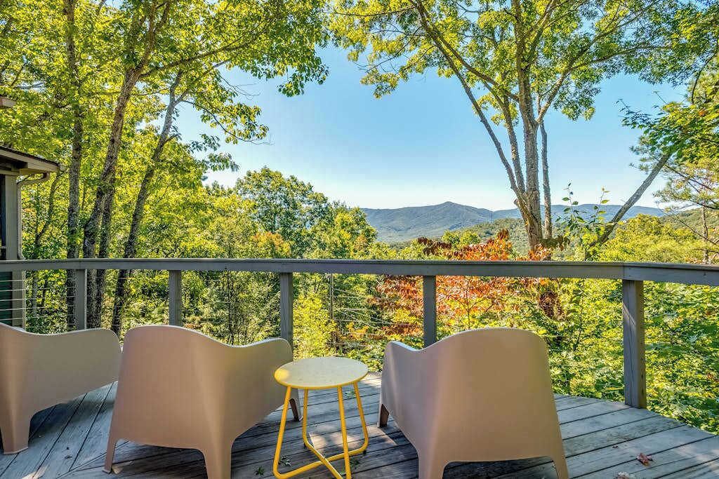 A deck with chairs and a table, overlooking a forested landscape with mountains in the distance.