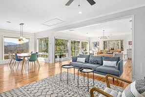 Ein geräumiges Wohnzimmer mit grauem Sofa, Esstisch und Stühlen, große Fenster mit Blick ins Freie.