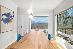 Ein Konferenzraum mit Holztisch, Stühlen, einem Gemälde und einem großen Fenster mit Blick auf die Berge.